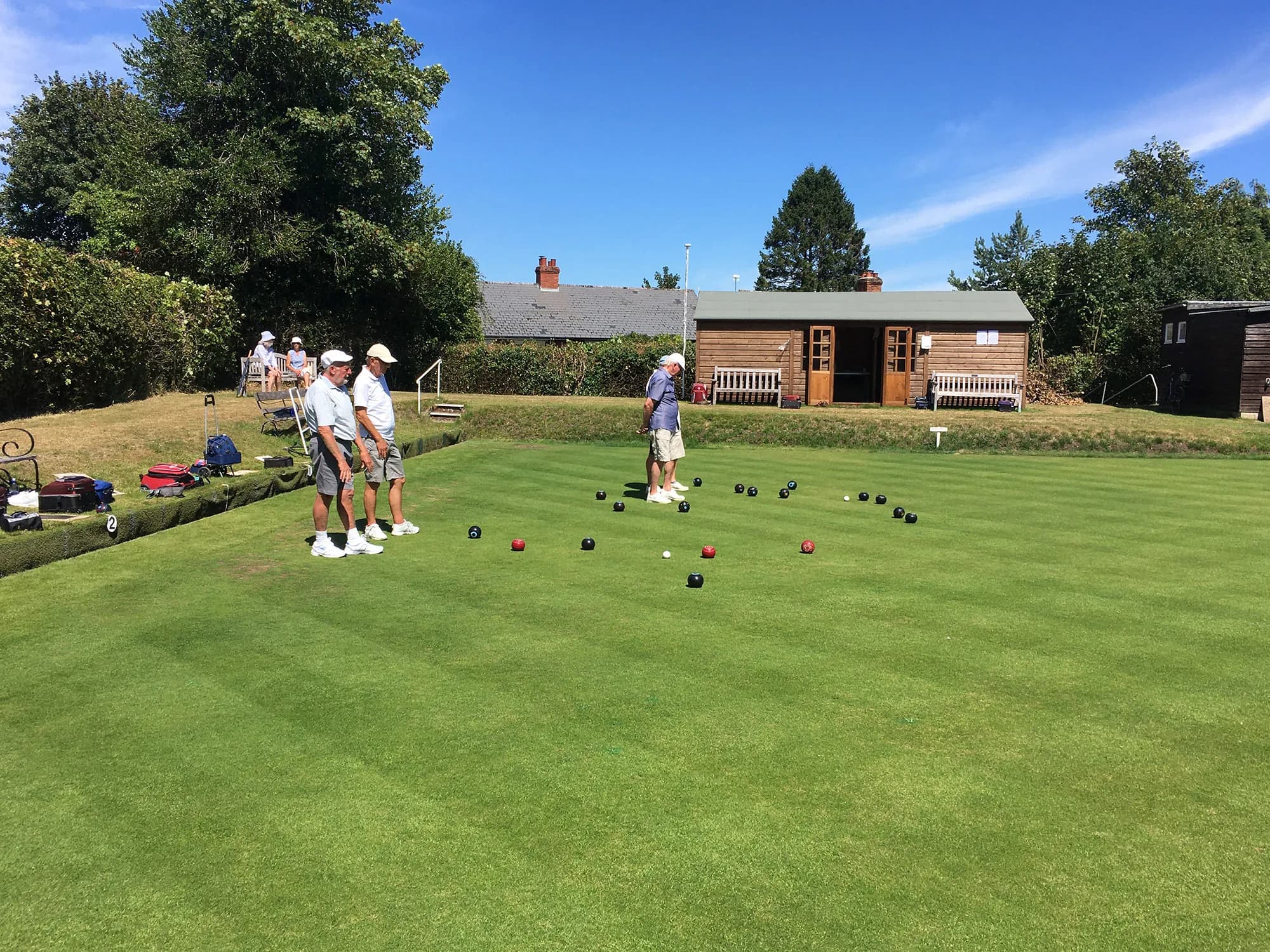 The five rink green at Midhurst Bowling Club on a summer afternoon, with the clubhouse beyond